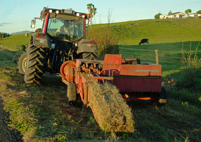 Farmer operating a tractor and hay baler in a New Zealand paddock